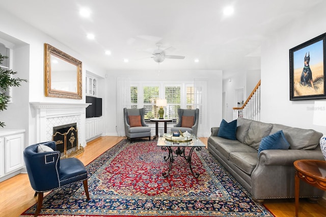 living room featuring ceiling fan, a tiled fireplace, stairway, light wood-type flooring, and recessed lighting