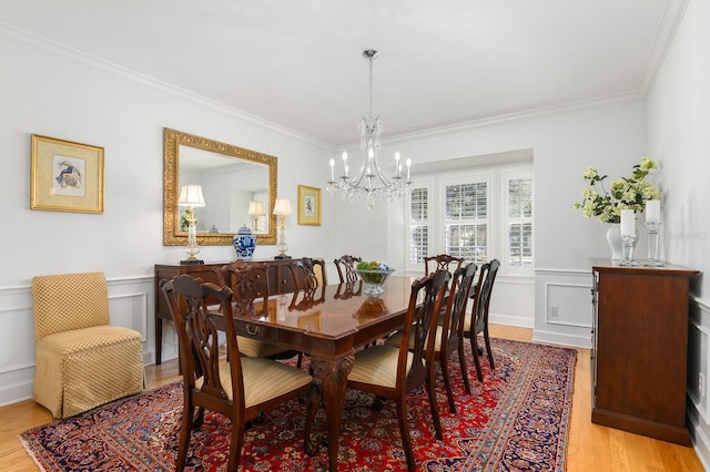 dining space with a wainscoted wall, a notable chandelier, light wood-style flooring, crown molding, and a decorative wall