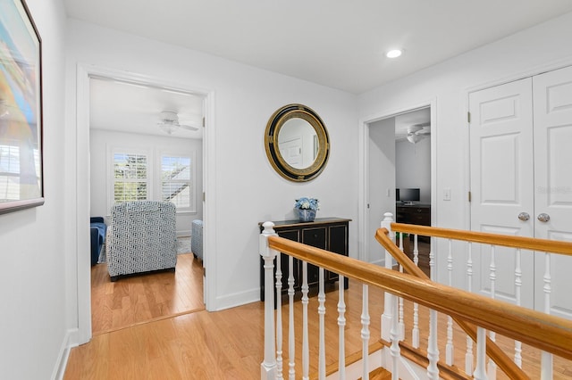 hallway with an upstairs landing, recessed lighting, light wood-style flooring, and baseboards