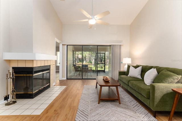 living room featuring light wood-style flooring, a fireplace, high vaulted ceiling, and ceiling fan