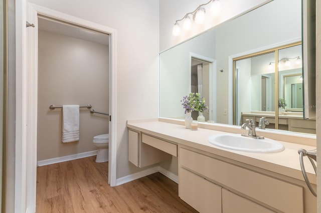 bathroom featuring toilet, baseboards, wood finished floors, and vanity