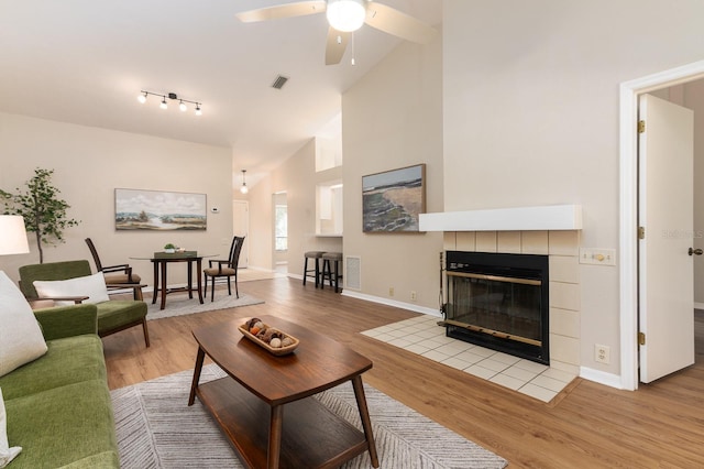 living area with visible vents, wood finished floors, high vaulted ceiling, a tile fireplace, and baseboards