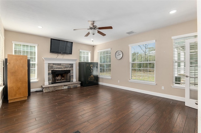 unfurnished living room with dark wood-style flooring, visible vents, ceiling fan, a stone fireplace, and baseboards