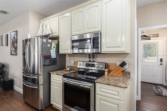 kitchen featuring appliances with stainless steel finishes, dark stone counters, dark wood-style flooring, and visible vents