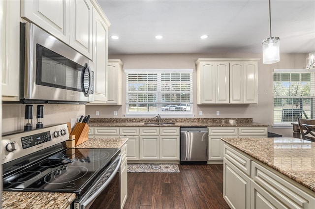 kitchen featuring hanging light fixtures, light stone countertops, stainless steel appliances, white cabinetry, and a sink