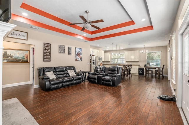 living room with baseboards, a raised ceiling, dark wood-style flooring, and ceiling fan with notable chandelier