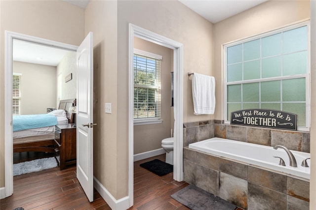 ensuite bathroom with baseboards, toilet, ensuite bath, wood finished floors, and a bath