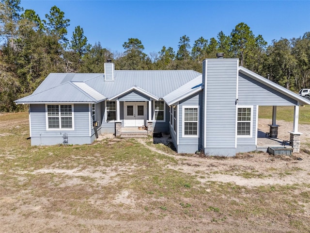 back of property featuring a porch, a chimney, metal roof, and a yard