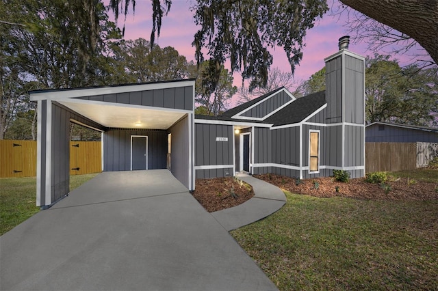 view of front of home featuring a yard, concrete driveway, board and batten siding, fence, and a carport