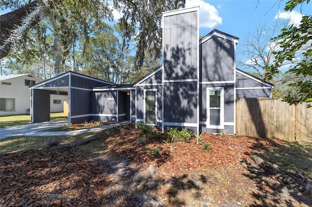 view of front facade featuring a carport, driveway, a chimney, and fence