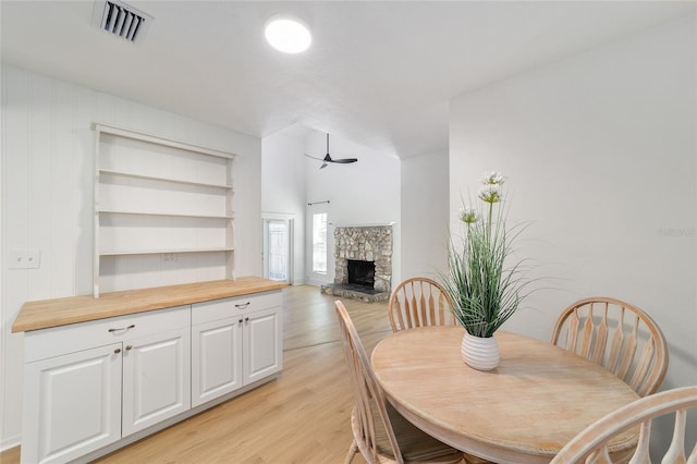 dining area with light wood-style flooring, a fireplace, visible vents, and a ceiling fan