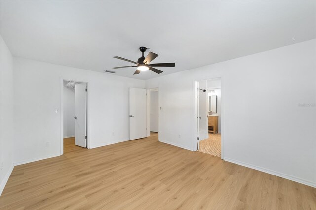 unfurnished bedroom with light wood finished floors, visible vents, baseboards, ensuite bath, and a walk in closet