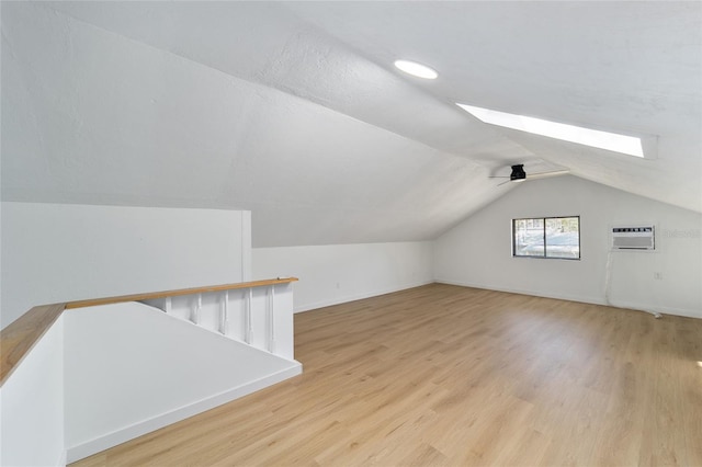 additional living space with lofted ceiling with skylight, a wall mounted air conditioner, wood finished floors, and baseboards