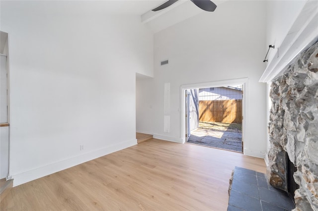 unfurnished living room with light wood-style floors, visible vents, beam ceiling, and a stone fireplace