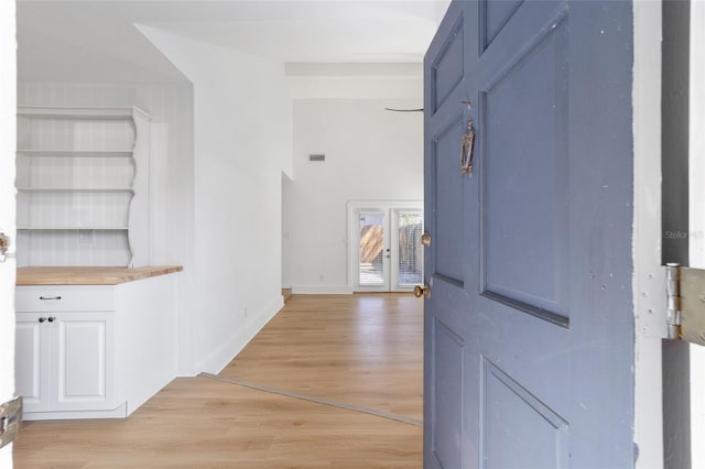 hall with visible vents, light wood finished floors, a towering ceiling, and baseboards