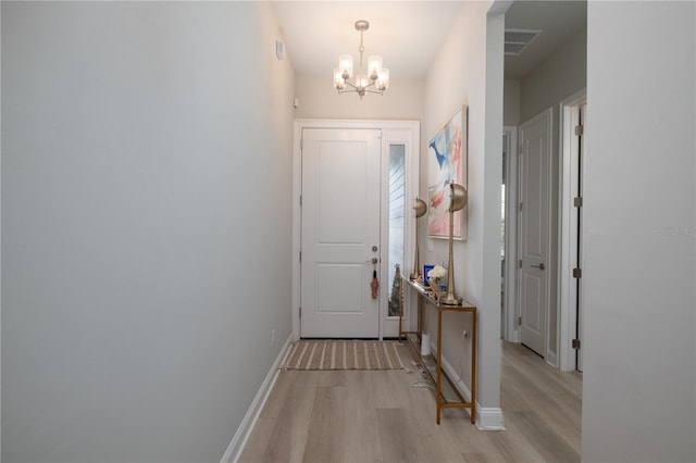 doorway to outside featuring baseboards, visible vents, a notable chandelier, and light wood finished floors