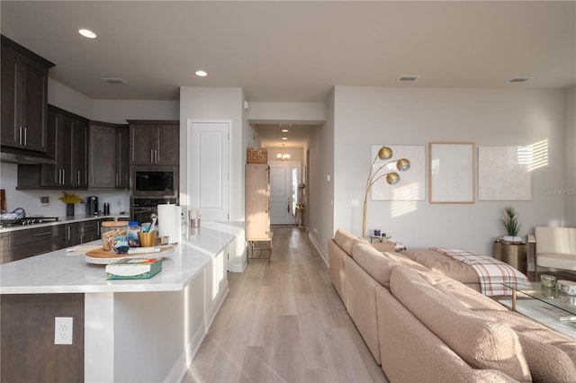 kitchen featuring light stone counters, light wood finished floors, appliances with stainless steel finishes, open floor plan, and dark brown cabinets