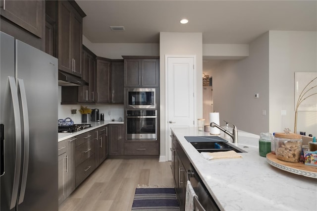 kitchen with light wood-style flooring, dark brown cabinetry, under cabinet range hood, a sink, and appliances with stainless steel finishes