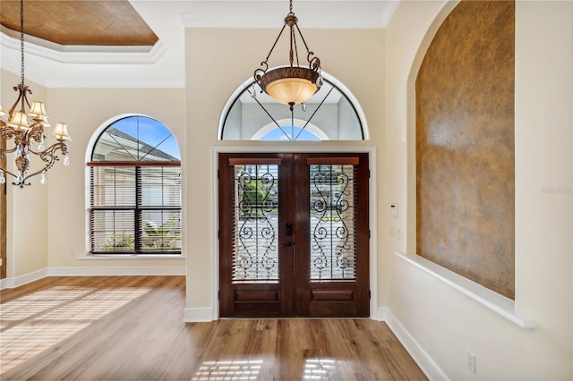 entryway featuring wood finished floors, baseboards, arched walkways, crown molding, and a notable chandelier