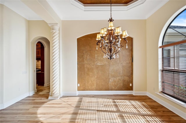 interior space with a notable chandelier, ornamental molding, wood finished floors, arched walkways, and a raised ceiling