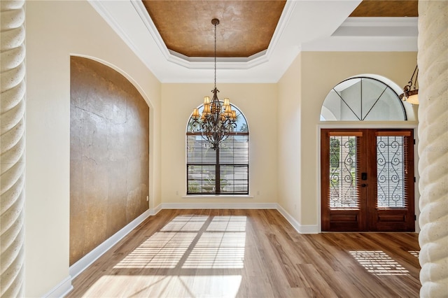 entrance foyer featuring an inviting chandelier, a raised ceiling, crown molding, and wood finished floors