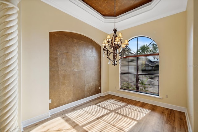 unfurnished dining area with ornamental molding, an inviting chandelier, wood finished floors, arched walkways, and a raised ceiling