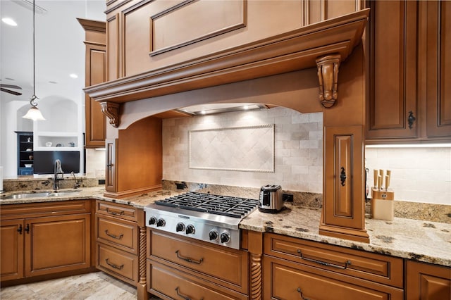 kitchen with a sink, light stone counters, brown cabinetry, and stainless steel gas cooktop