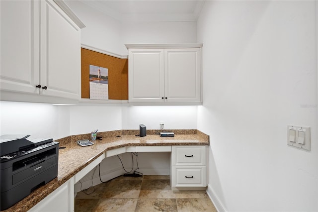 office space featuring stone finish floor, baseboards, built in desk, and ornamental molding