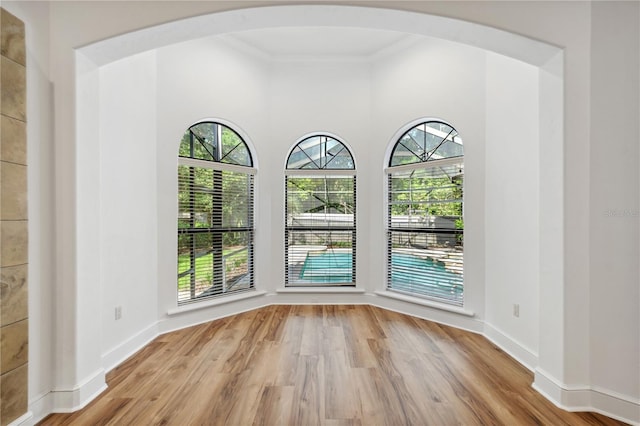 unfurnished room featuring baseboards, arched walkways, and wood finished floors