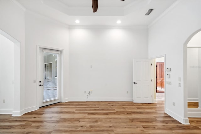 spare room with light wood finished floors, visible vents, arched walkways, a raised ceiling, and a ceiling fan