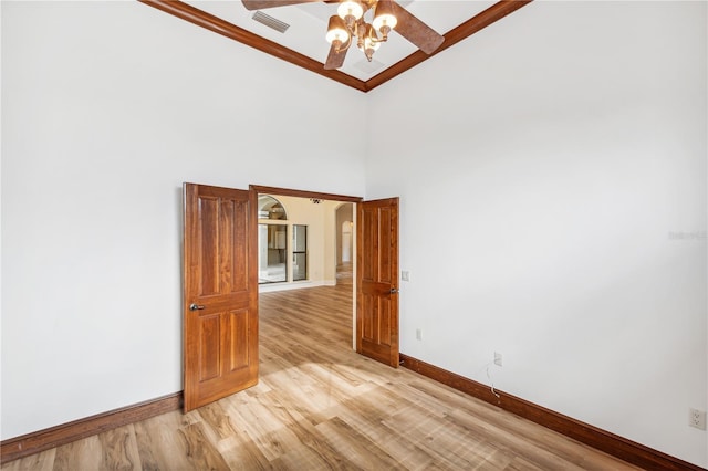 unfurnished room featuring visible vents, a towering ceiling, light wood finished floors, baseboards, and ceiling fan