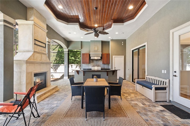 view of patio with a glass covered fireplace, outdoor dining space, exterior kitchen, and ceiling fan