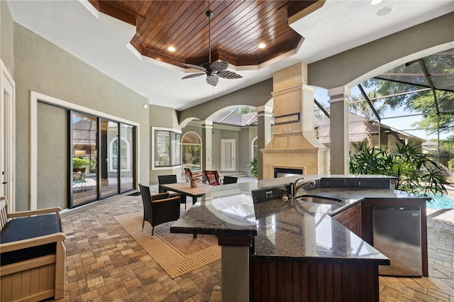 view of patio with a large fireplace, a lanai, outdoor dining area, a ceiling fan, and a sink