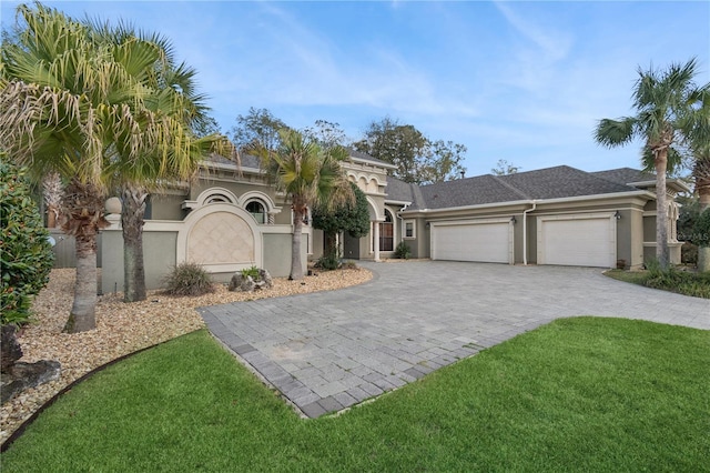 view of front facade featuring a front yard, roof with shingles, stucco siding, decorative driveway, and a garage