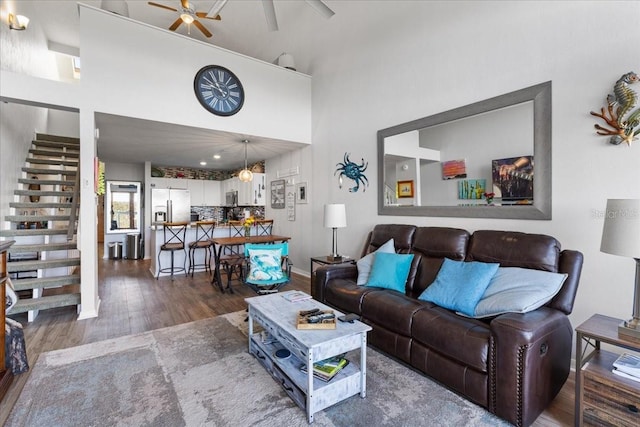 living room featuring stairs, ceiling fan, a high ceiling, and dark wood-style flooring