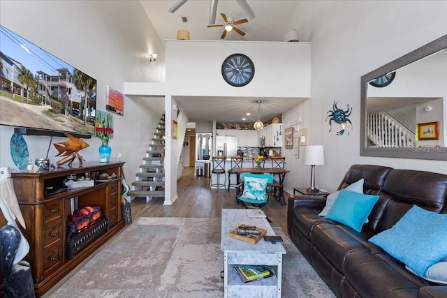 living area with a towering ceiling, ceiling fan, stairway, and wood finished floors