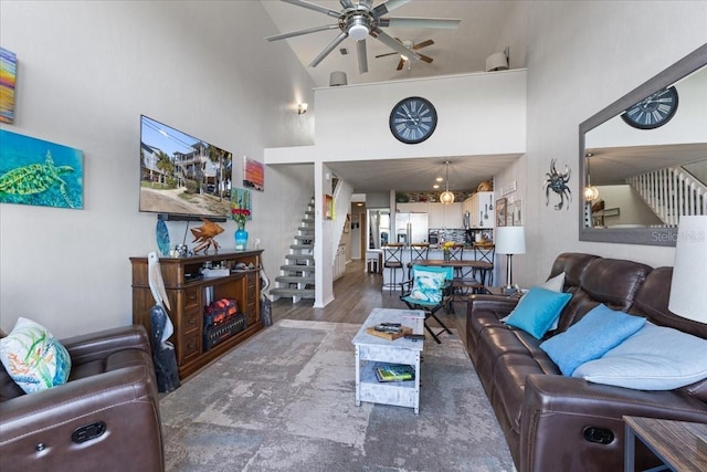 living area with stairs, ceiling fan, wood finished floors, and a towering ceiling