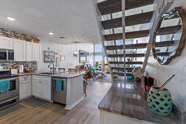 kitchen featuring dark wood finished floors, backsplash, appliances with stainless steel finishes, a sink, and a peninsula