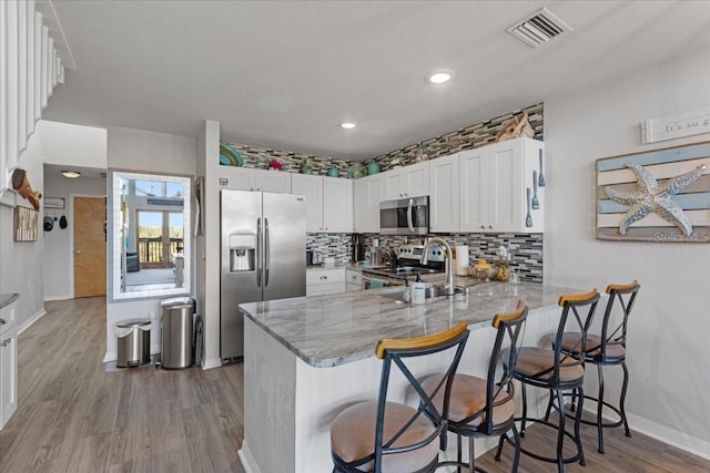 kitchen featuring visible vents, a peninsula, light stone countertops, stainless steel appliances, and light wood-type flooring