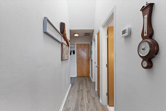 hallway featuring visible vents, light wood-style flooring, and baseboards