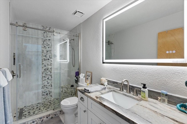 bathroom with a stall shower, visible vents, a textured wall, and toilet