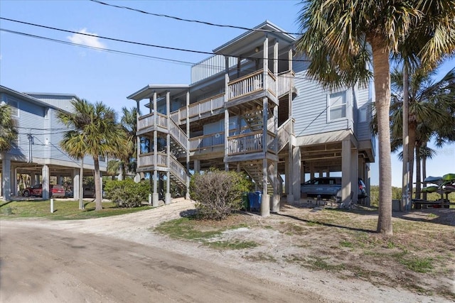 raised beach house featuring driveway, a balcony, stairs, and a carport