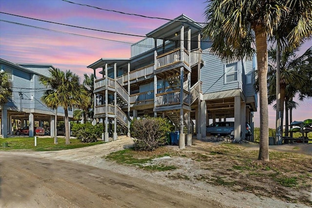 view of front of home with dirt driveway, a carport, and stairway