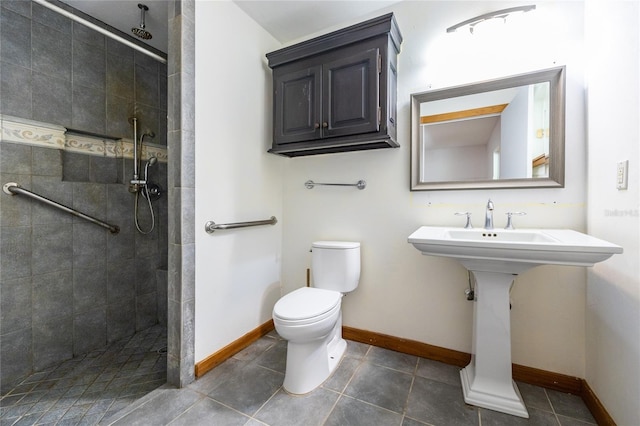 bathroom featuring tile patterned flooring, baseboards, toilet, a tile shower, and a sink