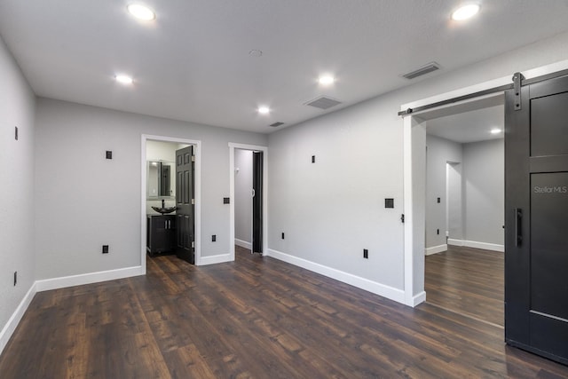 unfurnished bedroom with baseboards, a barn door, visible vents, and dark wood-style flooring