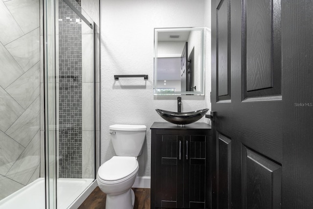 full bath with a textured wall, toilet, vanity, wood finished floors, and tiled shower