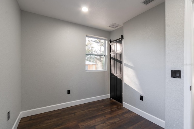 spare room with a barn door, dark wood-type flooring, visible vents, and baseboards