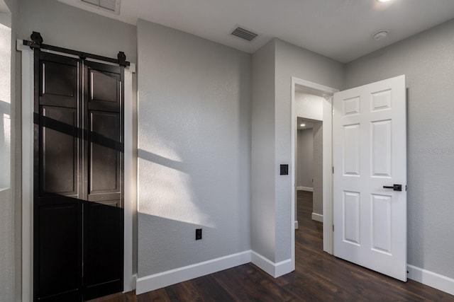 unfurnished bedroom with baseboards, a barn door, visible vents, and dark wood-type flooring