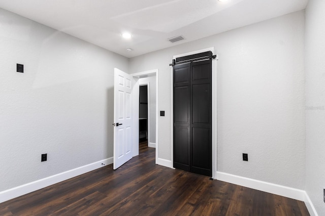 unfurnished bedroom with a barn door, dark wood-type flooring, visible vents, and baseboards