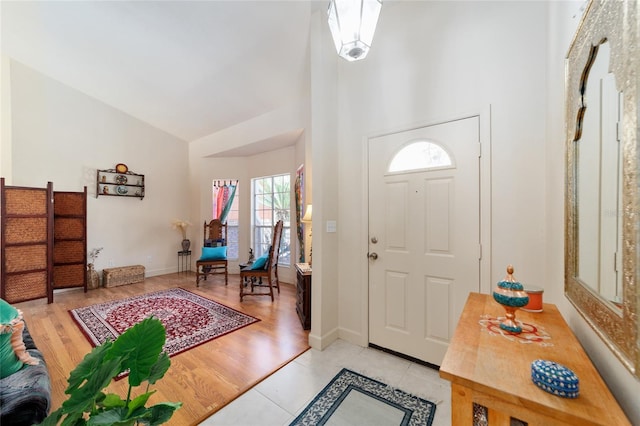 foyer entrance with high vaulted ceiling, light wood-style flooring, and baseboards